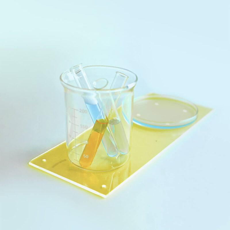 Glasgefäß mit zwei gefüllten Reagenzgläsern - Symbolbild für Gefahrstoffmanagement