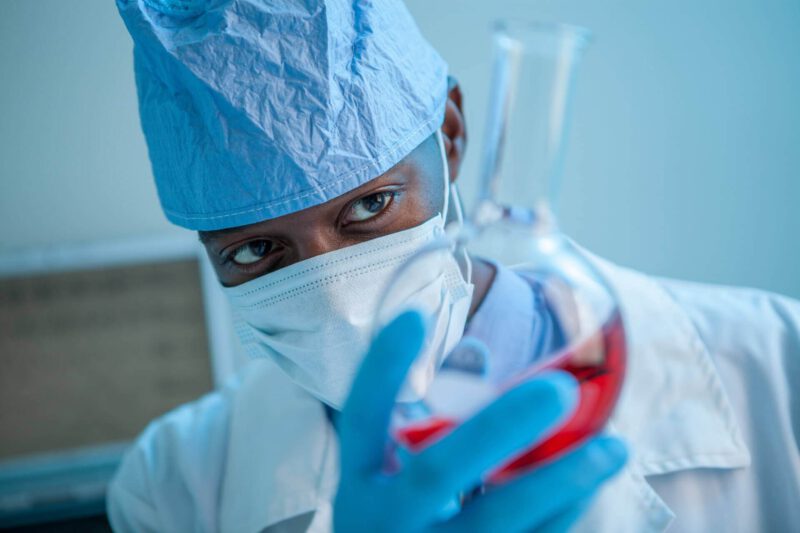 Laborant blaue Schutzkleidung Maske Glaskolben rote Flüssigkeit in Hand